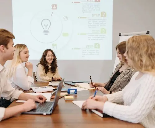 A team working around a table on laptops in front of a powerpoint.